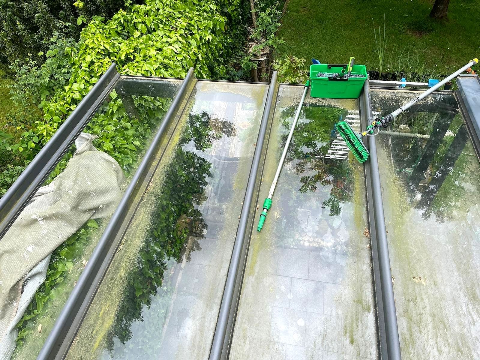 Reinigung eines Glasdachs mit Teleskopstange, Bürste und Eimer.